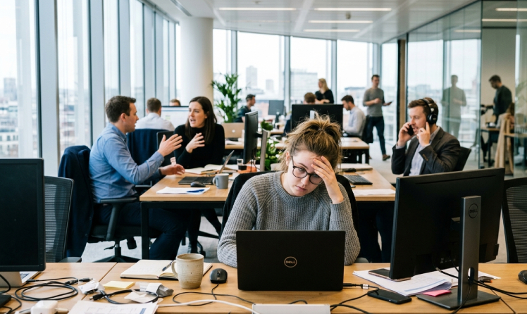 salariée fatiguée et déconcentrée par le bruit en open space avec collègues en arrière plan